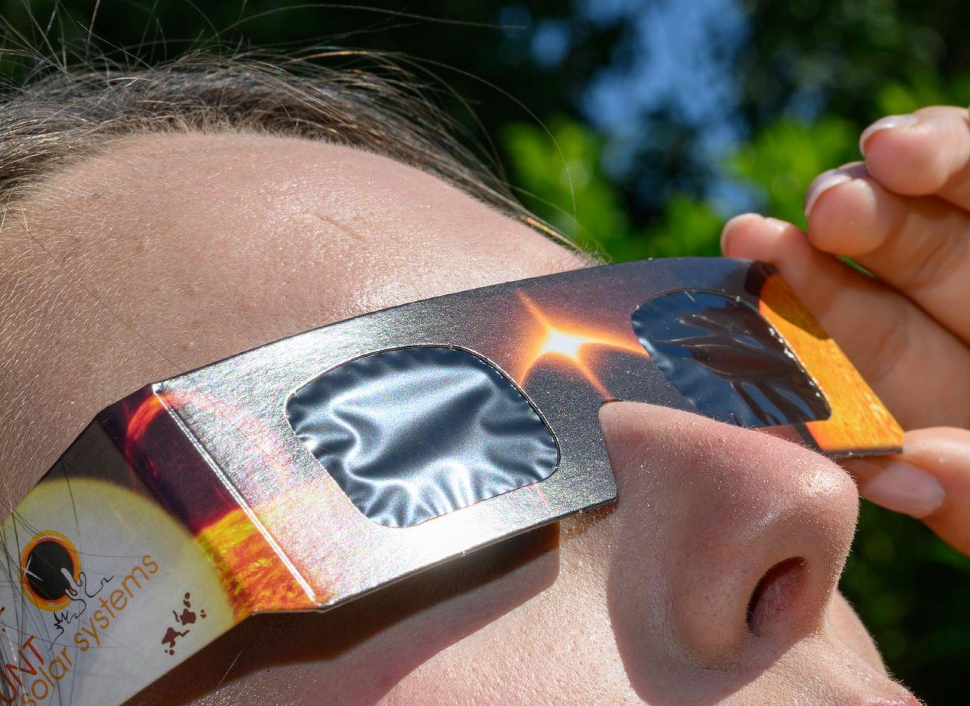 Eine junge Frau schaut durch eine Sonnenfinsternisbrille und betrachtet die Mittagssonne. (Bild: Patrick Pleul/dpa)