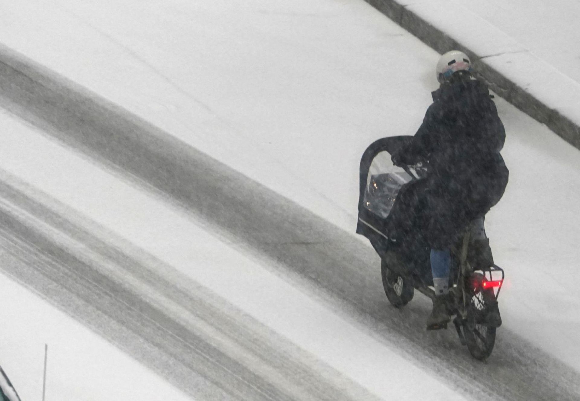 Eine Frau fährt mit einem Lastenfahrrad in Hamburg über eine verschneite Straße. (Bild: Marcus Brandt/dpa)