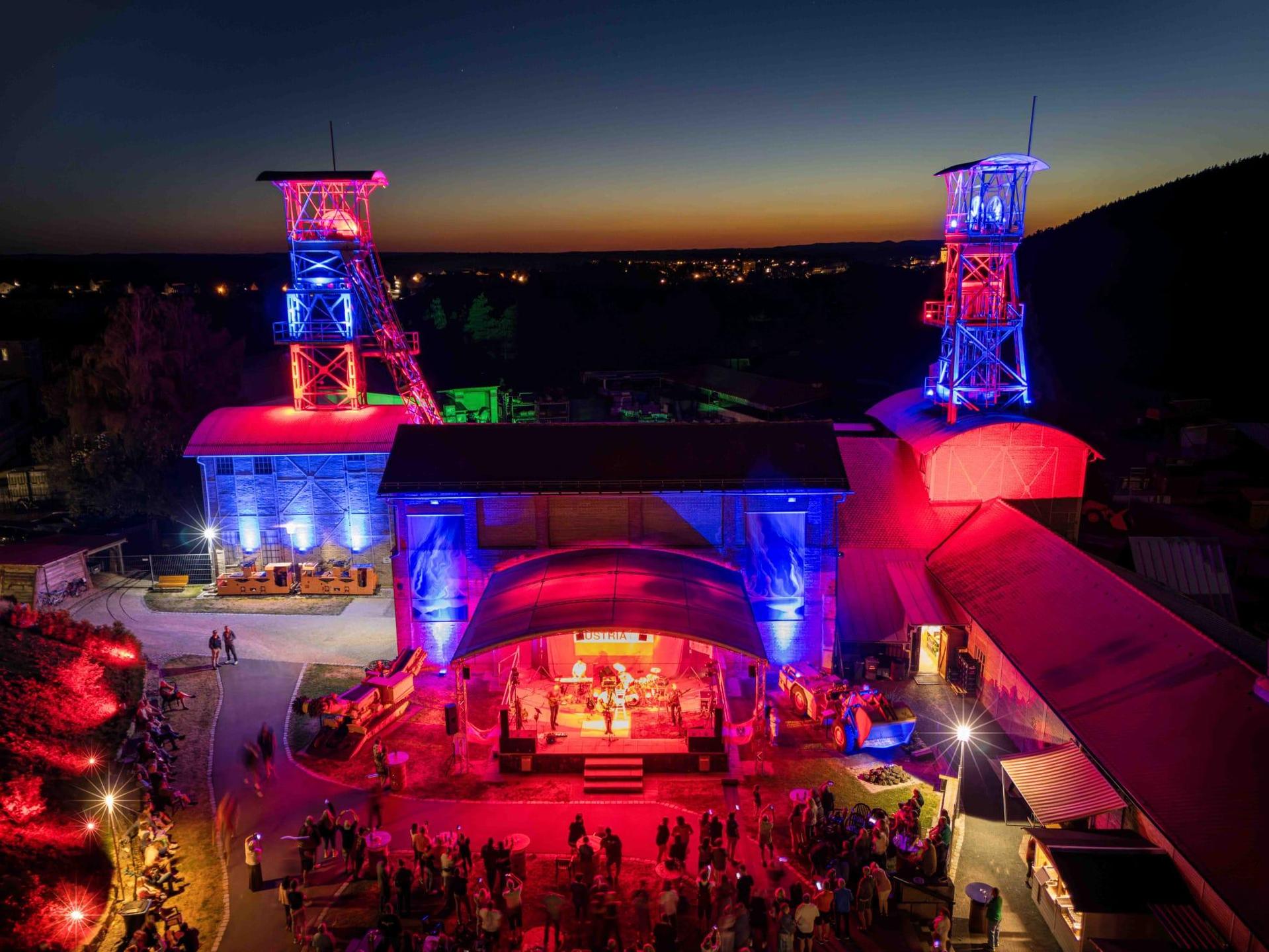 Das Classic-Rock-Festival G:O:A findet auf dem Gelände des Bergbaumuseums Maffeischächte statt. Neben der Bühnenbeleuchtung werden in der Dämmerung auch die Fördertürme illuminiert. (Bild: Michel Grüner / Förderverein Maffeispiele)